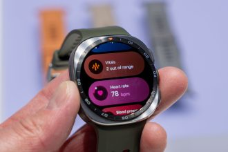 Photo officielle de la Samsung Galaxy Watch 9 tenue en main, écran affichant les widgets santé (vitals, fréquence cardiaque, tension)