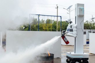 Robot humanoïde tenant un extincteur et déchargeant de la poudre sur un feu réel lors de l'exercice de lutte contre l'incendie des World Humanoid Robot Games à Pékin